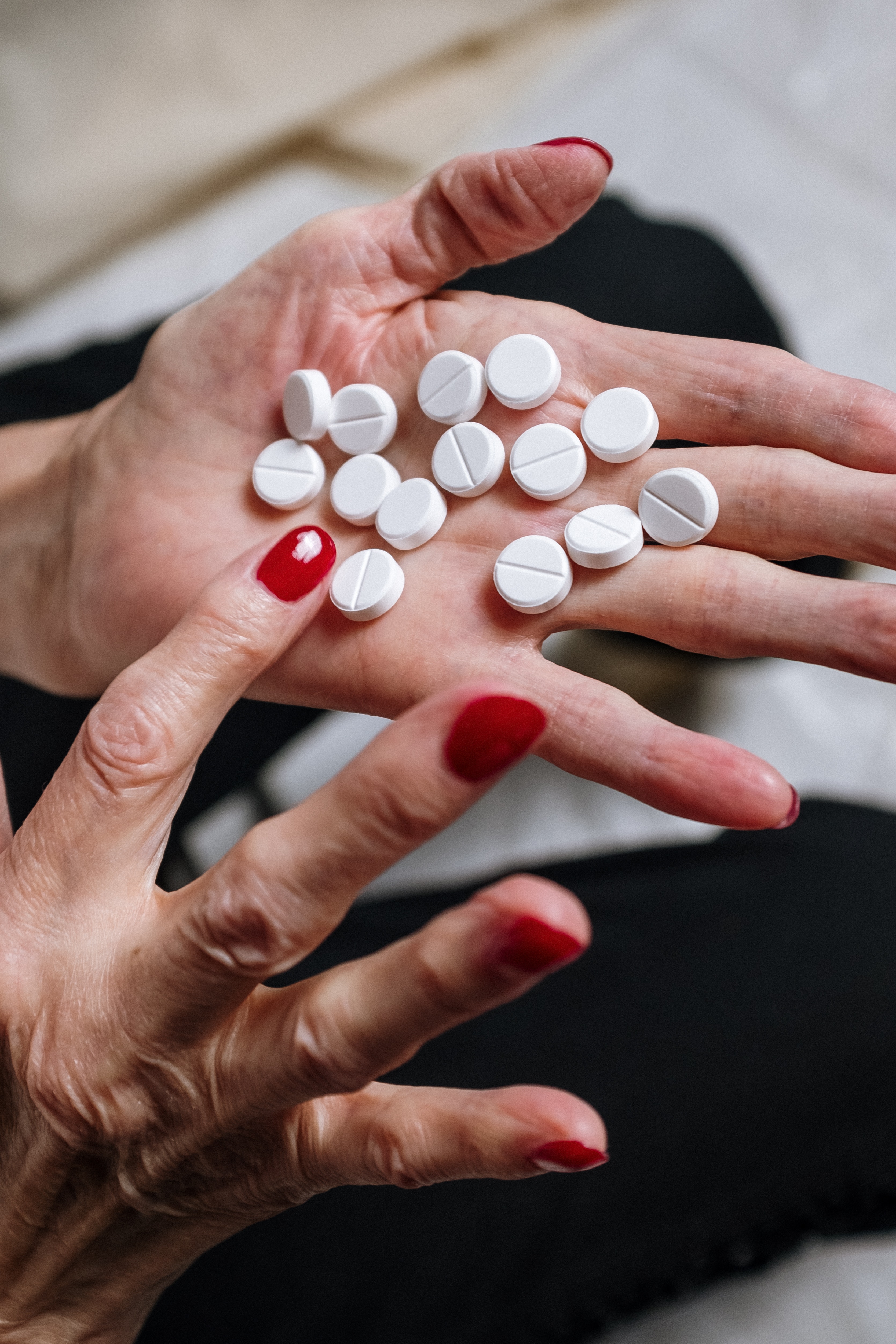 I en hand ligger ett tiotal vita piller och personen räknar hur många det är som ligger där genom att peka på pillren. Personen har rött nagellack.