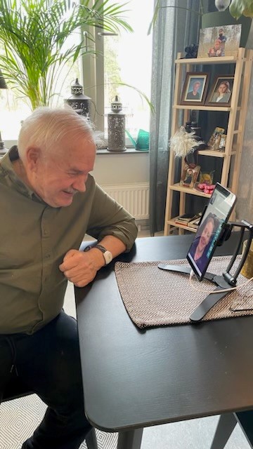 Bild på Rolf som sitter vid sin läsplatta och pratar med en anhörig, han ler stort